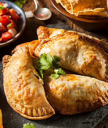 Golden chicken empanadas served with salsa and tortilla chips on a rustic surface.