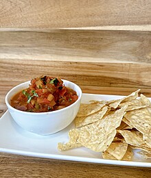 Fresh tortilla chips with chunky tomato salsa on a white plate over rustic wooden table.