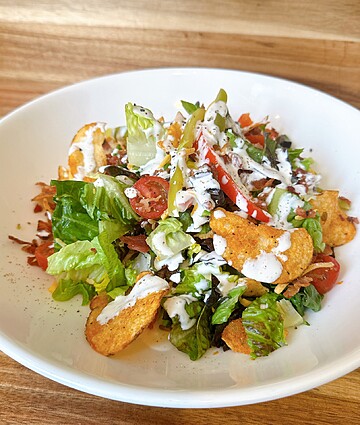 Colorful garden salad with fresh greens, cherry tomatoes, crunchy tortilla chips, and creamy dressing.