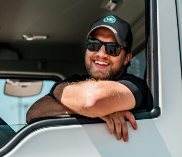 Professional food delivery driver smiling from truck cab, representing reliable foodservice logistics and wholesale distribution transportation services.