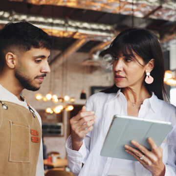 Professional food industry consultant discusses wholesale operations and supply chain management with colleague using tablet in modern warehouse facility.