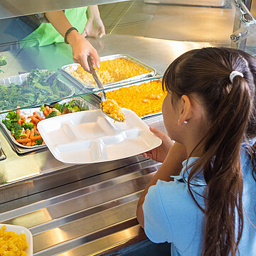 Young girl eagerly awaits a healthy lunch in a vibrant school cafeteria.