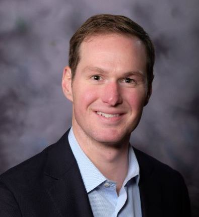 Confident young professional in tailored suit, smiling warmly for corporate networking.