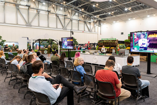 Culinary trade show food demonstration with seated audience in a bright convention hall.